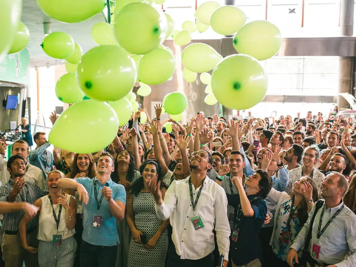 Hundreds of students cheering as green balloons drop over a crowded hall.